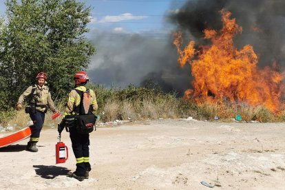 Dos bomberos al lado de una llamarada del incendio.