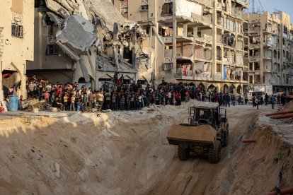 Vecinos miran cómo una excavadora trabaja en el lugar donde miembros de las Brigadas Al Qassam, el brazo militar del movimiento Hamás, buscan los cuerpos de rehenes israelíes.