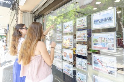 Dos personas miran los anuncios en el escaparate de una inmobiliaria en Tarragona.