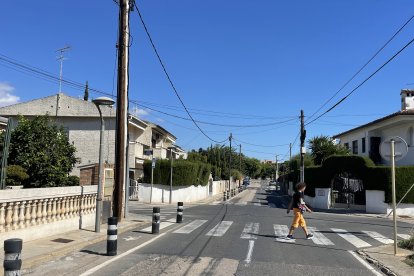 La calle tiene aceras estrechas, postes de luz y grietas y baches en el asfalto.