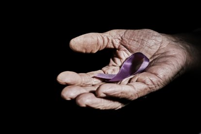 closeup of a senior caucasian woman with a purple ribbon in her hand against a black background