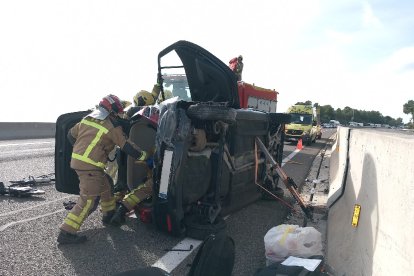 El coche volcado y los bomberos trabajando.