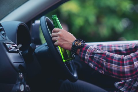 Hombre sosteniendo una botella de cerveza mientras conduce un coche