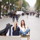 Dos jóvenes sentadas en una silla y un banco del primer tramo de la Rambla Nova de Tarragona