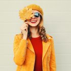 Autumn mood! happy smiling woman holding in her hands yellow maple leaves hiding her eye over gray wall background