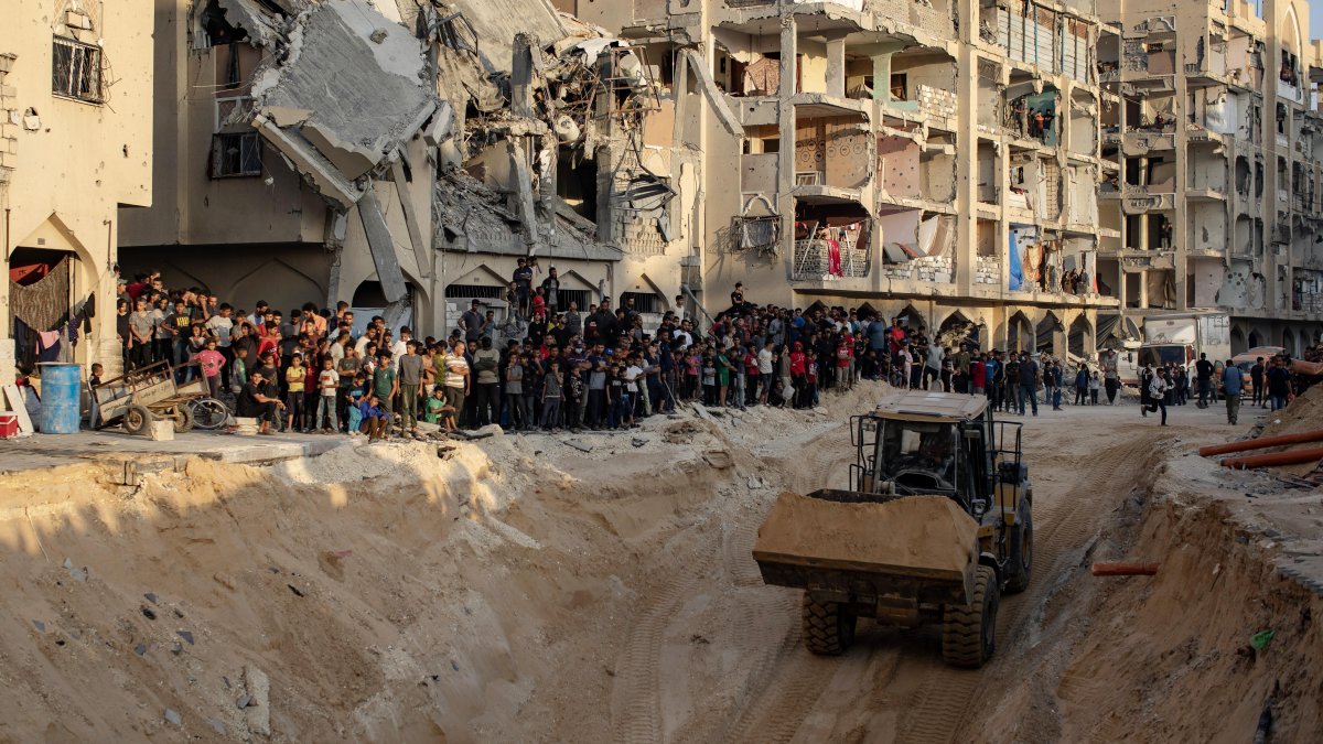 Vecinos miran cómo una excavadora trabaja en el lugar donde miembros de las Brigadas Al Qassam, el brazo militar del movimiento Hamás, buscan los cuerpos de rehenes israelíes.