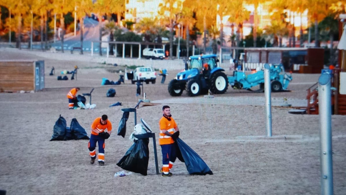 Operarios limpiando la arena antes de las siete de la mañana en l'Arrabassada.