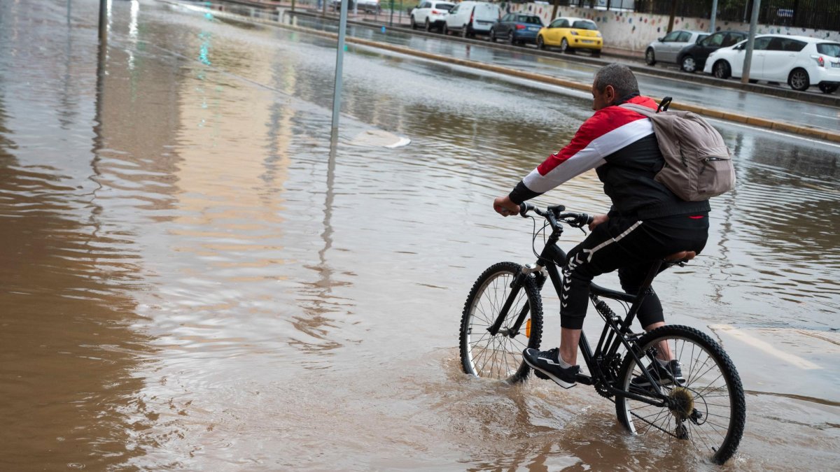 Una persona en bicicleta con la calle inundada.