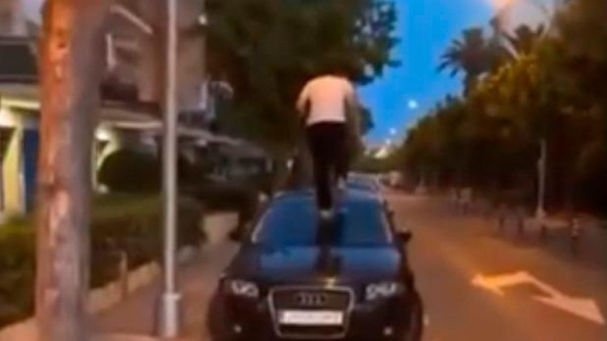 Frame del vídeo de un jóven subido al capó de un BMW negro.