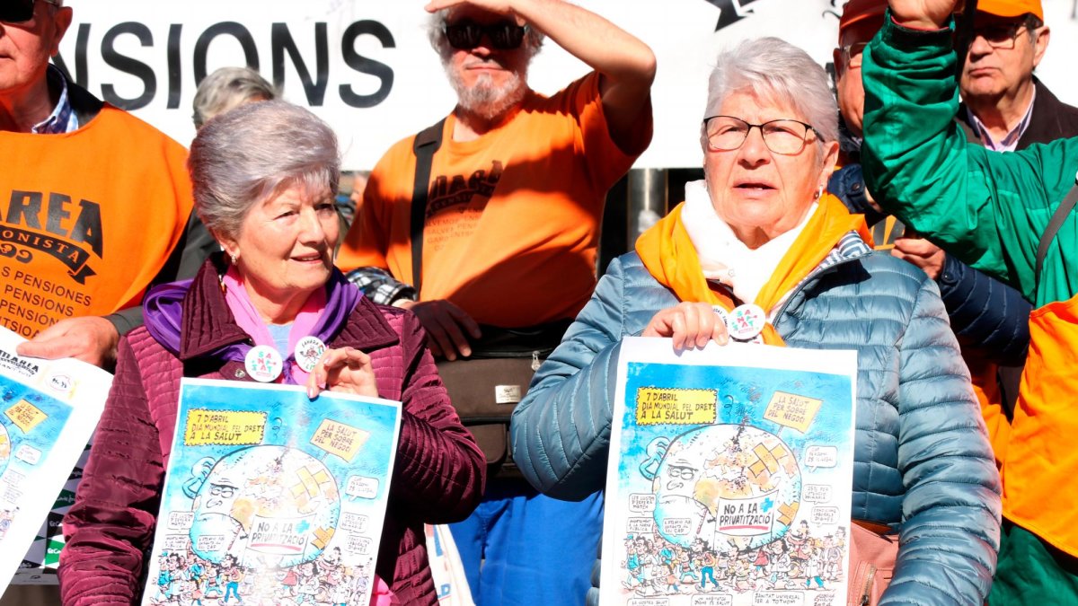 Dos miembros de Marea Pensionista de Catalunya mostrando el cartel que anuncia la manifestación de este domingo, 7 de abril, en el marco del Día Mundial de la Salud.