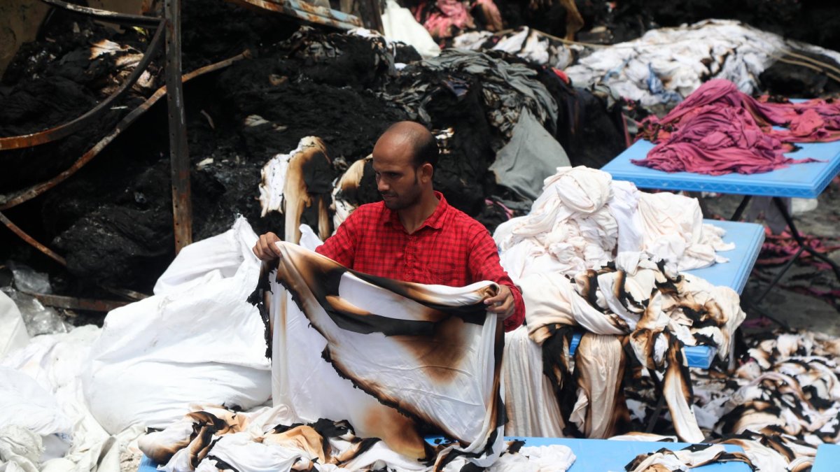 Un trabajador textil en la capital de Bangladés, Daca, intenta salvar tejidos tras el incendio de la factoría por los disturbios, en julio.