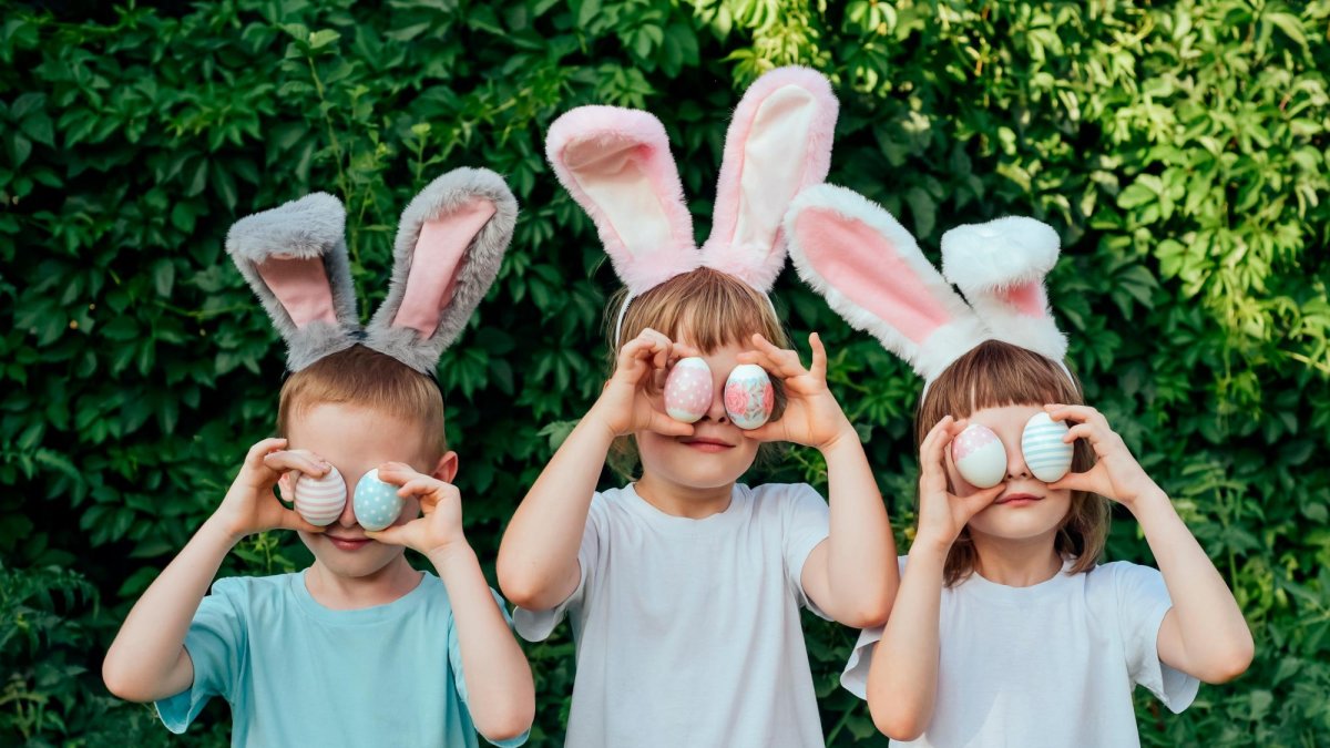 Tres niños disfrazados con orejas de conejo juegan con huevos de Pascua.