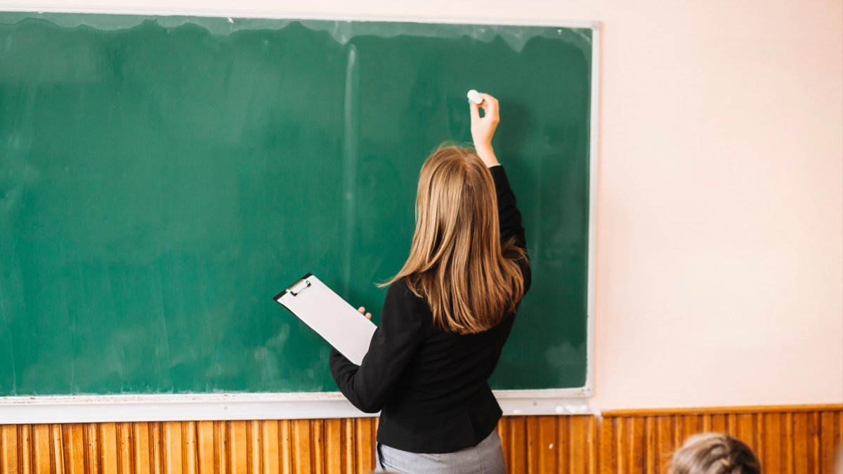 Una profesora escribe en la pizarra, en una