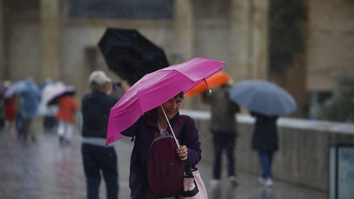 Una mujer intenta mantener su paraguas abierto bajo una intensa lluvia con viento.