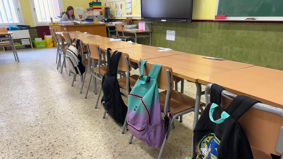 Una imagen de un aula con las mochilas de alumnos colgadas en el respaldo de la silla.